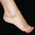 A close-up captures a foot wearing the Mega Lucky Charm Anklet Bracelet, crafted from 14k gold-filled material and featuring multiple amulets such as a heart, horseshoe, and feather. Renowned for offering evil eye protection and good luck with its eleven exclusive charms, the anklet stands out against a black background, while red-painted toenails enhance its beauty.